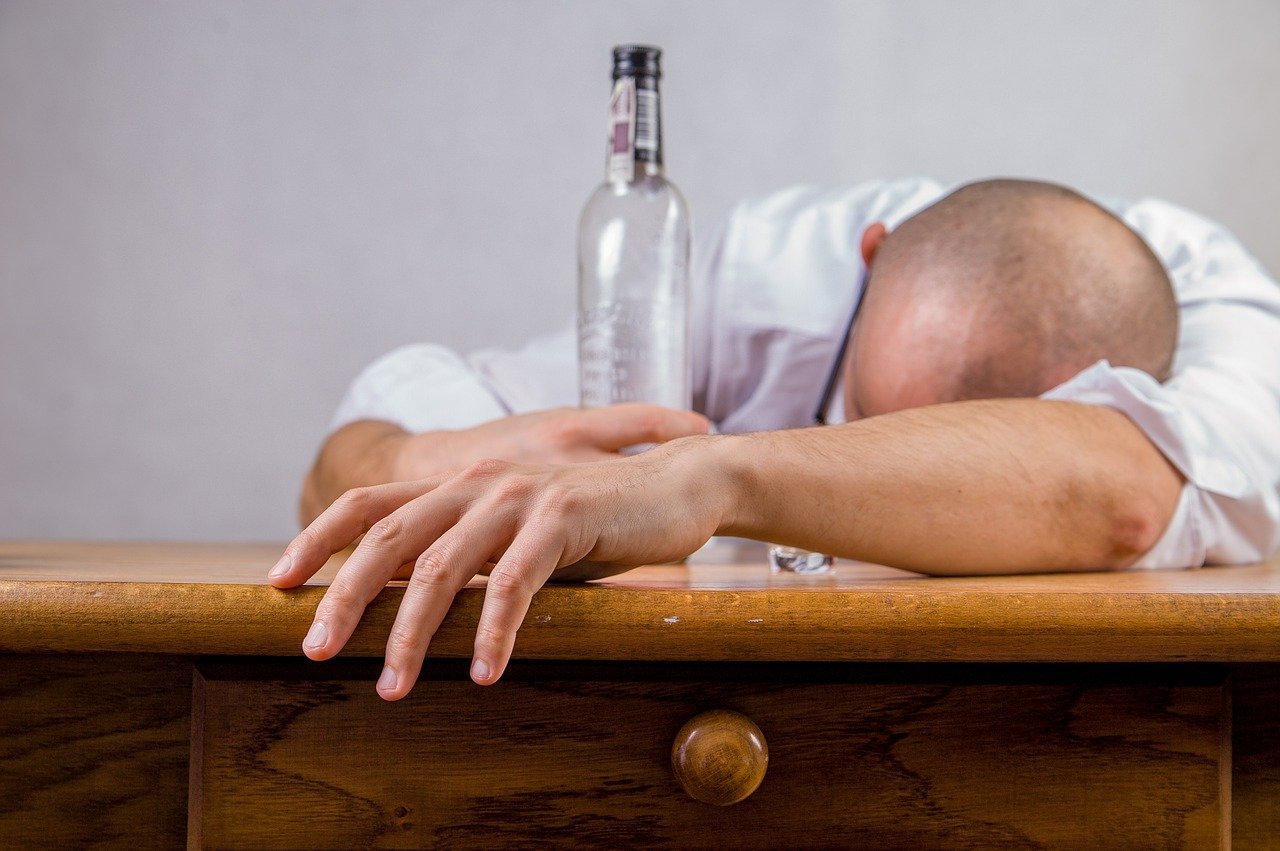 Pijany mężczyzna leżący na stole z butelką alkoholu